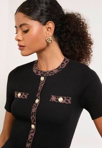 Musta ribbiknitti topp, millel on leopardimustriga aktsendid kaelas ja taskutes ning kuldsed nupud. Kujunduses on lühikesed varrukad.