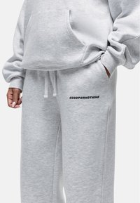 Grijze sweatshirt en trainingsbroek set, gemaakt van zacht fleecemateriaal, met een relaxte pasvorm, een kangoeroezak, en "GOODFORNOTHING" tekst op de broek.