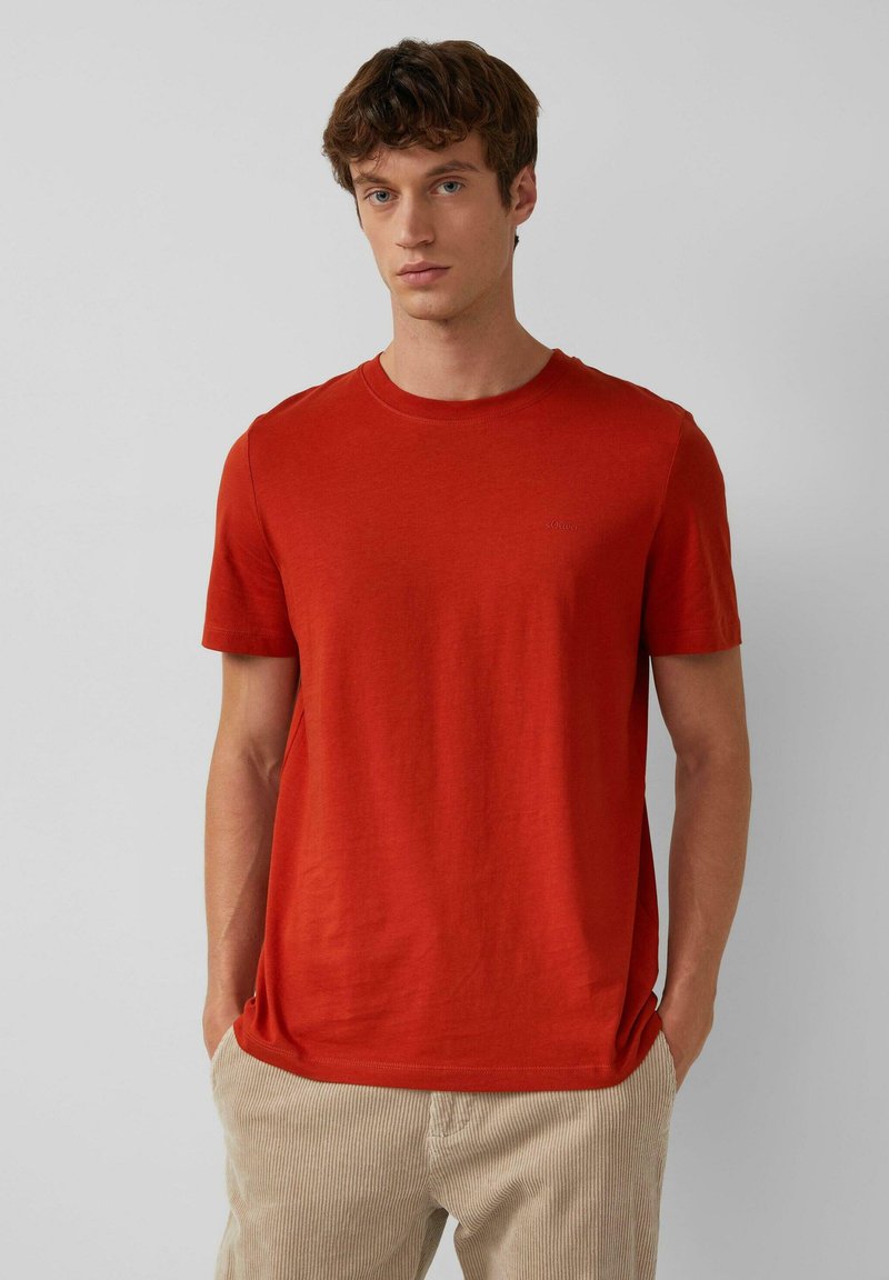 Rotes Baumwoll-T-Shirt mit kurzen Ärmeln und Rundhalsausschnitt, das ein dezentes Logo auf der Brust trägt. Weicher Stoff und lässige Passform.