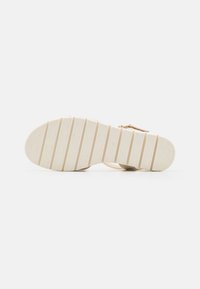 Beige sandal sole with ribbed surface, featuring a textured pattern and slight arch. Straps visible along the edges.