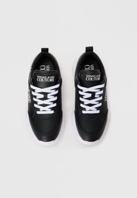 Črne usnjene superge z belimi vezalkami, ki imajo belo gumijasto podplato ter blagovno znamko na jeziku in strani. Minimalističen dizajn z gladko teksturo.