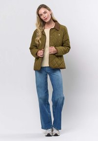 Olīvzaļš dūnu jaku ar brūnu apkakli un pogu slēdzeni, kopā ar krēmkrāsas džemperi un zilajām džinsām. Sudraba krāsas sporta apavi papildina apģērbu.