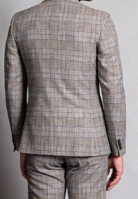 Completo a quadri beige con tessuto testurizzato, caratterizzato da piccoli dettagli blu. Design slim-fit con spalle strutturate e pantaloni su misura.