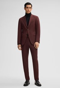 Abito due pezzi bordeaux con vestibilità su misura, blazer a un bottone e pantaloni con frontale piatto. Indossato sopra un dolcevita nero e scarpe nere.