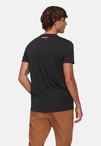 Zwarte t-shirt met korte mouwen en een ronde hals, met een wit "Mammut" logo op de bovenrug. Zacht katoenen materiaal, casual pasvorm.
