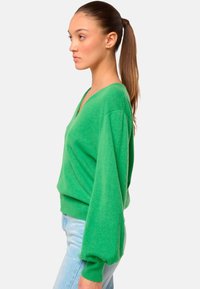 Pull vert en tricot doux, avec un col en V, des manches ballon et un ourlet ajusté. Assortie à un jean bleu clair.