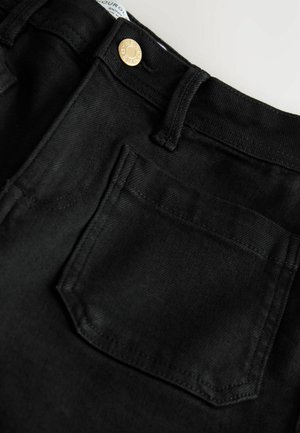 Schwarze Jeans aus Denim verfügen über ein klassisches Fünf-Taschen-Design mit einem goldenen Knopfverschluss. Die Textur ist glatt mit leichtem Stretch.