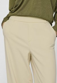 Beige op maat gemaakte broeken met een zachte textuur, voorzien van zijzakken en een vlakke voorkant, gecombineerd met een donkergroen top.
