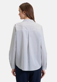 White long-sleeve shirt with navy vertical stripes, featuring a classic collar, button cuffs, and a back pleat for ease of movement.