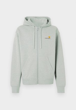 Lys grå zip-hoodie med en frontlomme, ribbede manchetter og et lille orange logo på venstre bryst. Lavet af blødt, tekstureret stof.