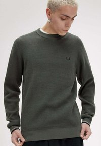 Maglione a maglia strutturata verde scuro con colletto e polsini a coste. Presenta un piccolo emblema sul petto e un orlo dritto.
