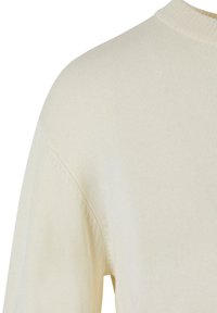 Pull en maille couleur crème montrant l'épaule et le haut de la manche avec un col rond et une fine texture côtelée.