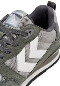 Szürke hálós felsőrésszel rendelkező sneaker, zöld velúrbetétekkel, fehér cikkcakk mintával, szürke fűzőkkel és párnázott gallérral. Kék címke van rajta logóval.