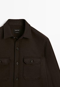 Donkerbruine button-up blouse met twee voorzakken met knopen en een kraag, gelabeld Massimo Dutti, plat neergelegd op een witte achtergrond.