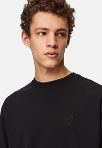 Black sweatshirt with a crew neck and textured cuffs, featuring an embroidered "Honesty Rules" logo on the chest. Soft fabric.