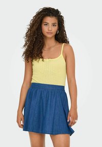Top in maglia gialla con spalline sottili, dotato di un piccolo fiocco, abbinato a una gonna di jeans blu scuro che si allarga leggermente all'orlo.