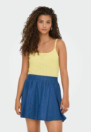 Top de tirantes fino amarillo de punto, con un pequeño lazo, combinado con una falda de mezclilla azul oscura que se ensancha ligeramente en el dobladillo.