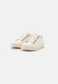 Ett par off-white låga canvas-sneakers med vita snören och gummisulor, uppvisade mot en vit bakgrund.