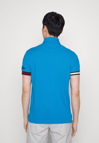 Blauwe polo met korte mouwen, voorzien van contrasterende rood en zwarte gestreepte manchetten. Glad materiaal en een klassiek kraagontwerp.
