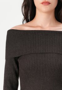 Off-the-shoulder, ribbed knit top in dark brown, featuring wide neckline and long sleeves. Texture is soft and fitted, emphasizing body shape.