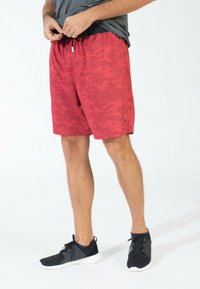 Pantalones cortos de camuflaje rojos con un patrón texturizado, cinturilla elástica y cordones. Combinados con zapatillas deportivas negras con suelas blancas.