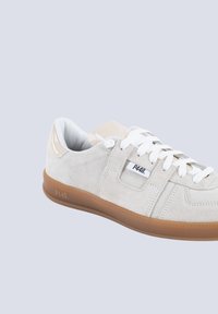Sneakers in suede grigio chiaro con lacci bianchi, un accento beige sulla linguetta e una suola in gomma naturale con dettaglio del logo sul lato.