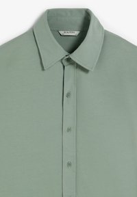 Camisa de botón verde claro con cuello clásico, fabricada en tejido suave, que presenta una tapeta de siete botones y un diseño liso.