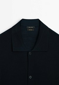 Dark navy button-up shirt made from merino wool. Features a flat collar and a smooth texture with five front buttons. Label visible inside.