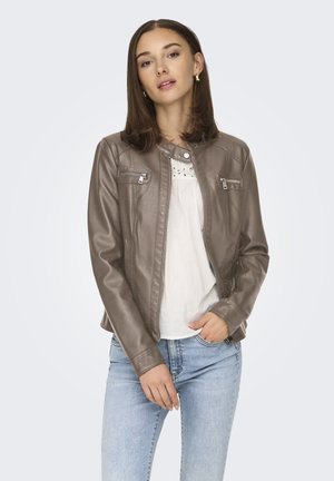 Chaqueta de cuero sintético marrón con un diseño ajustado, bolsillos en el pecho con cremallera y cuello a presión, llevada sobre una blusa blanca y jeans azules.