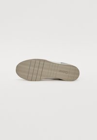 Shoe sole, hele beež kummist lainelise mustriga ja soontega. Lame disain, minimaalne tekstuur, keskel logo kanna lähedal.