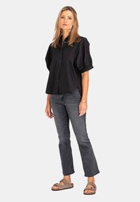 Schwarzes kurzärmliges Hemd mit Knöpfen und Puffärmeln, kombiniert mit dunkelgrauen gerade geschnittenen Jeans und braunen Riemensandalen.