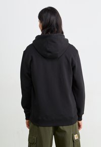 Schwarzer Kapuzenpullover mit Kängurutasche, gerippten Bündchen und Saum. Weicher Stoff, lässige Passform, getragen mit olivgrünen Cargo-Hosen.