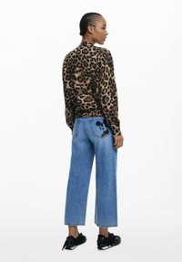 Pull en imprimé léopard en tissu doux, associé à un jean large bleu clair avec un patch de Mickey Mouse sur la poche arrière, et des baskets noires.