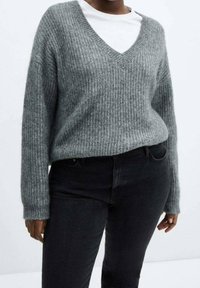 Szary sweter z prążkowanego materiału, z głębokim dekoltem w kształcie V, długimi rękawami i luźnym krojem, nałożony na biały T-shirt, w połączeniu z czarnymi dżinsami.