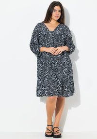 Schwarzes und weißes gemustertes Kleid mit V-Ausschnitt und Dreiviertelärmeln, das locker geschnitten ist und eine geraffte Taille hat, die über dem Knie endet.
