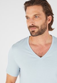 T-shirt di colore blu chiaro a V in morbido tessuto, con maniche corte e vestibilità rilassata, caratterizzato da cuciture minime e una texture liscia.