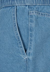 Gros plan sur un jean en denim bleu clair montrant la poche avant avec des coutures visibles et des détails de texture.