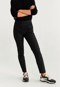Pantalon noir à motif à carreaux avec une coupe slim, présentant une texture lisse et une taille haute. Assorti à des baskets noires et blanches.