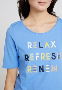 Vaaleansininen lyhythihainen t-paita, jossa on teksti "RELAX REFRESH RENEW" eri väreissä ja kuvioissa. Pehmeä puuvillamateriaali. Pyöreä kaula-aukko.