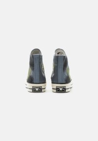 Sneaker alte in blu e verde con finitura texturizzata, suole in gomma, patch con logo sul lato, strisce a contrasto e etichetta nera distintiva.
