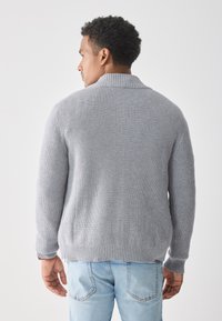 Grå stripet strikkegenser med sjalkrage og lange ermer, med en teksturert overflate og avslappet passform, kombinert med blå jeans.