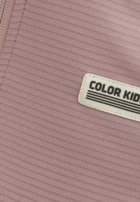 Ljust rosa tyg med en subtil textur, med en vit etikett som säger "COLOR KIDS" med svarta linjer på.