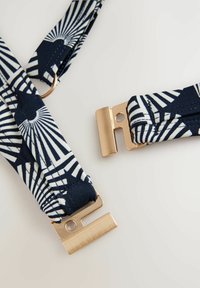 Marinblå och vita mönstrade hängslen med guldfärgade klipp. Tyget är slätt med geometrisk design och en blank yta på metalldetaljerna.