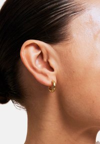 Gouden oorring in de vorm van een ring, gedragen aan een mensenoor, met een glad, gepolijst oppervlak en een ronde, compacte vorm.