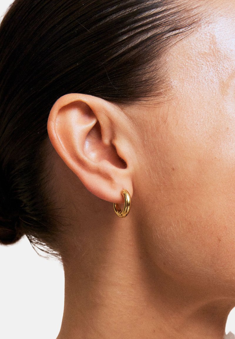 Gouden oorring in de vorm van een ring, gedragen aan een mensenoor, met een glad, gepolijst oppervlak en een ronde, compacte vorm.