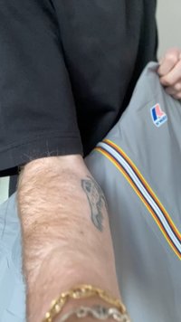 Person i svart skjorte som holder en grå jakke med rødt, gult og blått stripet kantbånd og en liten blå og rød logo nær skulderen.