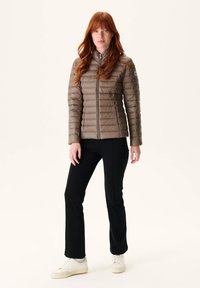 Lichtbruine gewatteerde jas met een hoge kraag, ritssluiting aan de voorkant en een slim fit ontwerp. Gecombineerd met zwarte slim fit broek en witte sneakers.