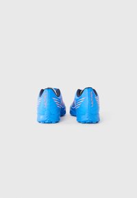 Une paire de chaussures de sport bleues avec des accents corail et le texte "ULTRA", vue de l'arrière sur un fond blanc uni.