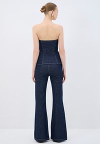 Top senza spalline in denim abbinato a jeans a campana, entrambi di colore blu scuro con cuciture a contrasto. Visibile la texture liscia e la vestibilità sartoriale.