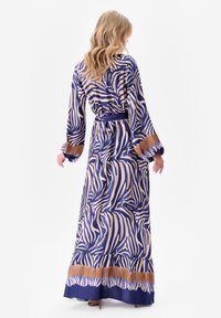 Maxi sukienka w niebiesko-kremowy wzór zebry. Posiada długie rękawy, wiązany w talii pas oraz warstwowy dół z kontrastującą brązową taśmą. Gładki materiał.